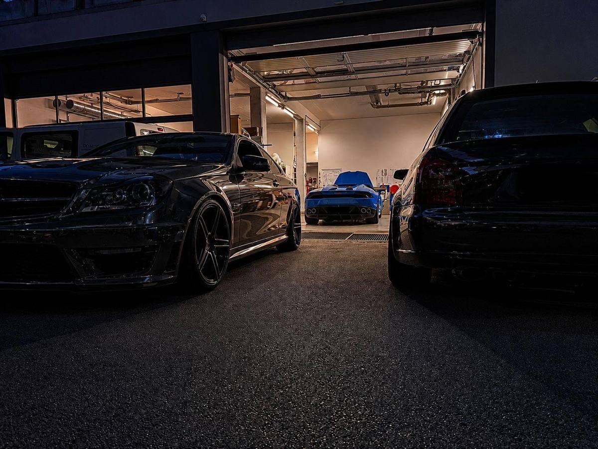 Werkstatt von AjPerformance am Abend mit Fahrzeugen vor der geöffneten Halle